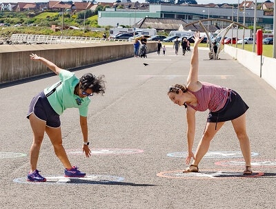 Two ladies stretching - pointing down to the ground and up to the sky