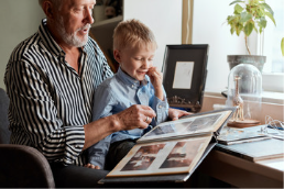 Little blonde boy around 5 years old sitting on an older man's lap and looking at a photo album