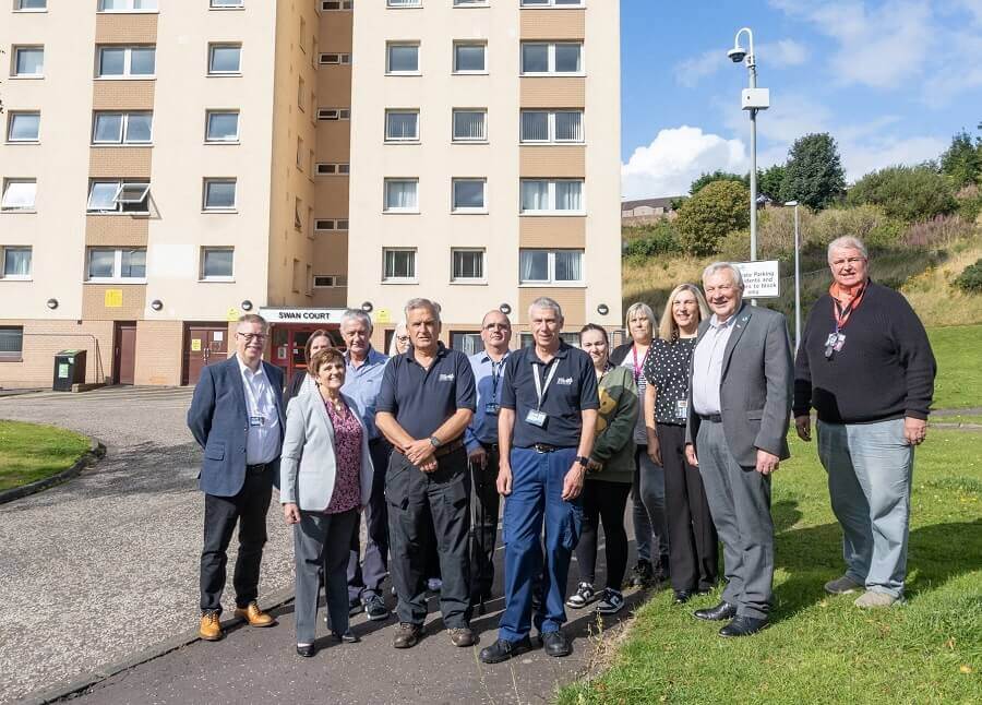 Group of people standing in front of a residential building labelled 'Swan Court' on a sunny day